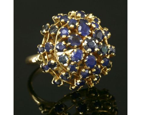 A Continental gold sapphire domed cluster ring,with a circular mixed cut sapphire, surrounded by four rows of graduated oval 