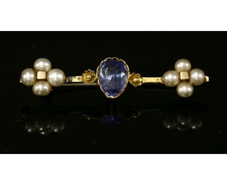 A late Victorian foiled sapphire bar brooch,with a pear cut sapphire, rub set to a plain collet, with a flower head at each s