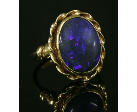 A gold single stone black opal ring, with an oval cabochon black opal, rub set to a plain collet.  A twisted flat wire border