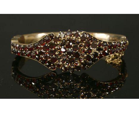 A Victorian bohemian garnet gilt metal hinged bangle,with a central cluster of graduated circular faceted garnets to split sh