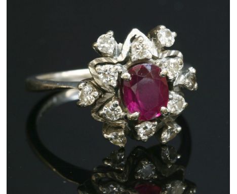 An 18ct white gold, ruby and diamond cluster ring, with an oval mixed cut ruby, four claw set to the centre.  A border of two