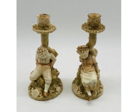 A pair of Royal Worcester candlestick figures by James Hadley of a boy and girl sitting upon a rock beneath a tree (c1890 - s