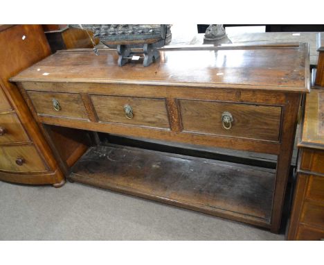 A Georgian oak dresser base fitted with three short drawers with brass lions head and ringlet handles, raised on plain suppor