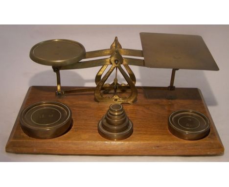 A set of brass Postal Scales on a oak plinth and seven weights, half ounce to 16 ounces.