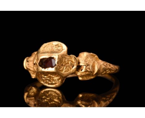 Ca. AD 1600 - 1700An ornate, gold ring with scrolled detailing to the shoulders, pyramidal bezel, and inset garnet to the cen