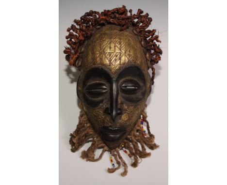 Decorative Tribal Art and the Eclectic Interior - a West African mask, stylised eliptical features, brass clad and chased wit