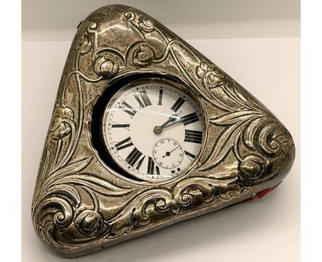 A heavy silver plated goliath bedside watch with enamelled dial set in a triangular shaped watch holder with embossed art nou