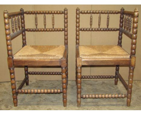 A pair of stained beechwood corner chairs with bobbin turned frames and drop in rush seats 