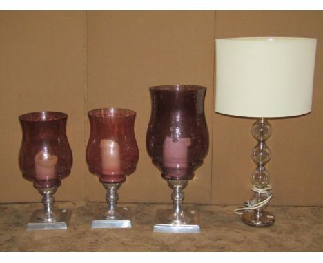 A pair of contemporary candle lanterns with amethyst tinted glass shades, set on resin (to simulate metal) stems, with square
