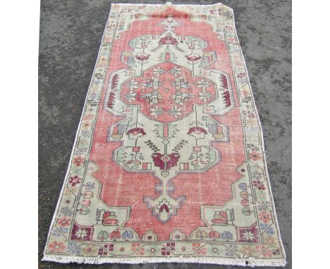 A Persian carpet with a stylised floral central medallion in hues of pink and cream.  220cm x 115cm approx. 