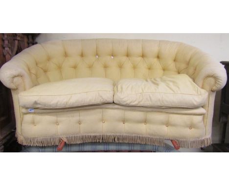 A small parlour room sofa with horseshoe shaped back and concave outline with buttoned finish in a pale lemon coloured uphols