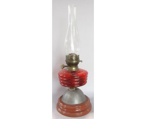 An oil lamp with a red ribbed glass font, lacks a shade. 