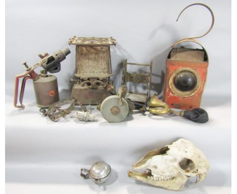 A miscellaneous collection of items including a sheep's skull, a rusty red roadside lantern, a rusty old blow torch, a distre