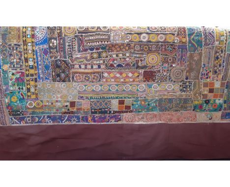 A large Indian textile panel featuring a mosaic of  embroidered  samples with a  burgundy red border and lining. 2.6x2.08m. 