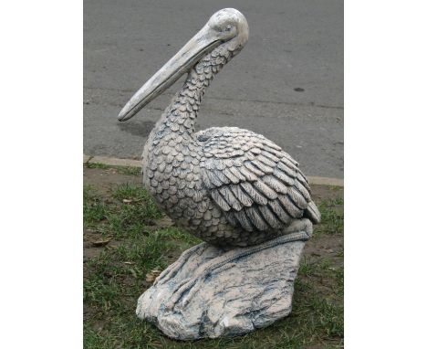 A painted and weathered composite garden ornament in the form of a pelican/stork seated on a rocky outcrop, 58 cm high togeth