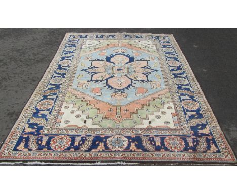 A Heriz carpet with a broad blue flower shaped central medallion on a pale cream ground, signed in a corner.  287cm x 192cm a