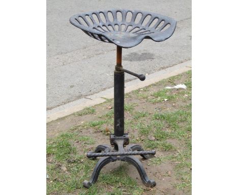A cast iron adjustable high stool with tractor type seat over a foot rest with swept and scrolled supports 
