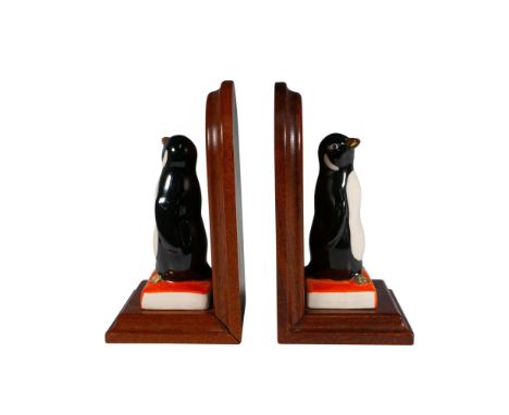 Two black and white penguins stand on orange books labeled Best Wishes atop wooden bases, each featuring a matching penguin l