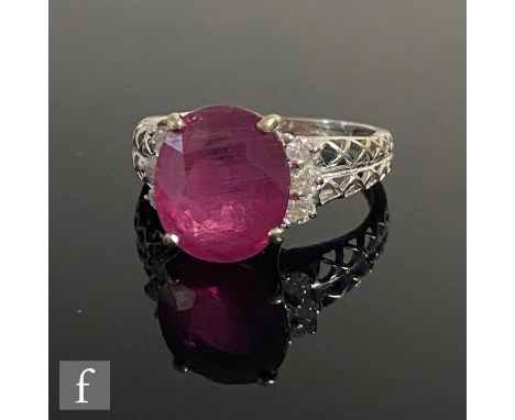 An 18ct hallmarked white gold ruby and diamond ring, central oval claw set ruby, length 11.5mm, flanked by three brilliant cu