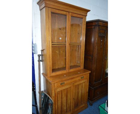 A TALL LIGHT OAK GLAZED TWO DOOR BOOKCASE with adjustable shelves above a single long drawer and double panelled doors, appro