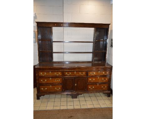 A GEORGE III OAK AND MAHOGANY BANDED DRESSER BASE, fitted with an arrangement of seven drawers surrounding central double doo