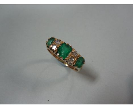 An Edwardian 18ct gold emerald and diamond ring, with three graduated cushion shaped emeralds separated by pairs of old round