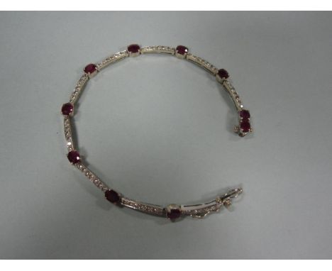 A ruby and diamond bracelet set in 18ct white gold, formed as an articulated line with ten oval cut rubies spaced by gently c