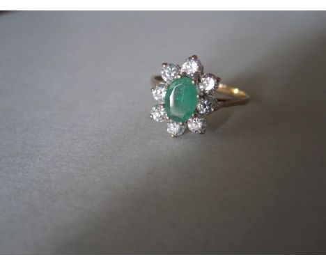 An emerald and diamond cluster ring set in hallmarked gold, the oval cut emerald claw set in a border of eight round brillian