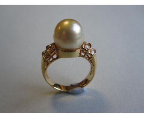 A pearl and diamond ring, set to the centre with a 10.2 mm diameter x 10.7mm high pearl of pale lemon yellow hue between curv