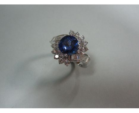 A tanzanite and diamond cluster ring, the round cut mid to deep indigo tanzanite four claw set in a crossover design, with cu