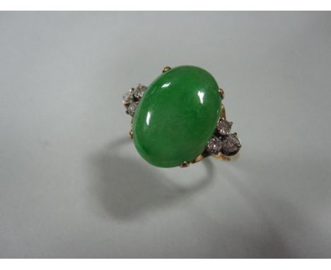 A jade and diamond ring, the oval cabochon mid green jade four claw set between trios of round brilliant cut diamonds to a sc