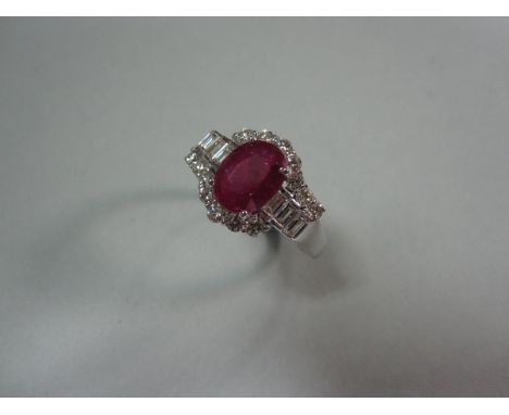A fracture filled ruby and diamond cluster ring, the oval cut ruby claw set in white precious metal between lines of baguette