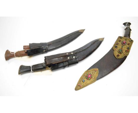 Three 20th Century Indo-Persian Kukri knives, one with horn handle and gilt mounted and glass cabochon set scabbard, the larg