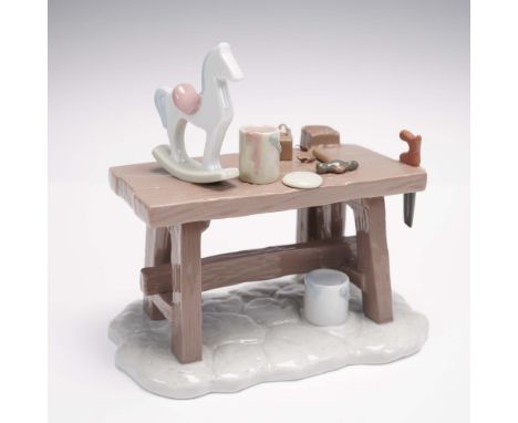 Depicts a meticulously detailed workshop scene. The figurine features a wooden workbench adorned with an assortment of miniat