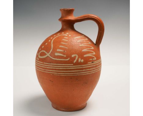 This terracotta jug features a warm orange clay body adorned with flowing white slip decoration in abstract and calligraphic 