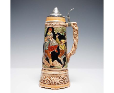 Vintage ceramic beer stein with a detailed raised-relief design featuring a traditional alpine scene on one side and a lively