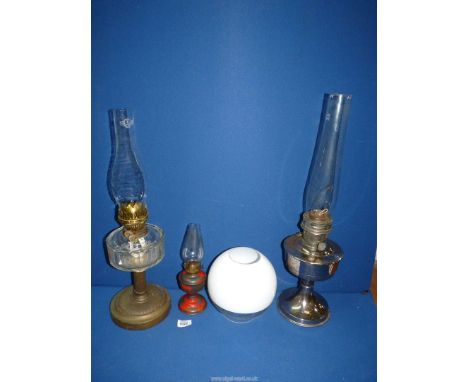 Three oil lamps including clear glass reservoir with brass base, chromed base and reservoir and small, red painted lamp, all 