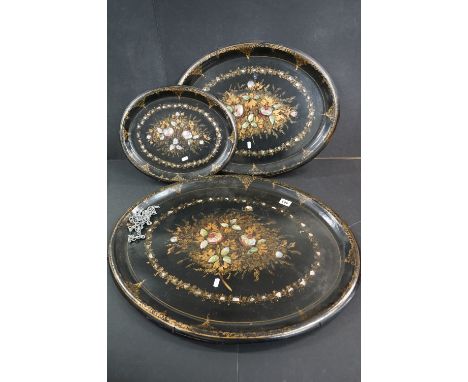 A group of three antique lacquered paper mache graduated trays with mother of pearl floral decoration. 