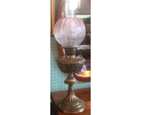 An Edwardian pressed brass paraffin lamp with cranberry tinted spherical shade.