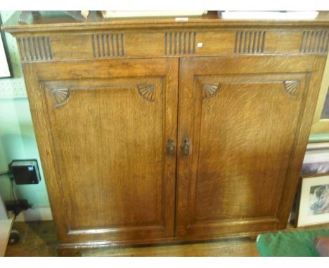 An early 20th century oak cupboard, having rectangular top over fluted frieze and a pair of panelled doors enclosing shelves 