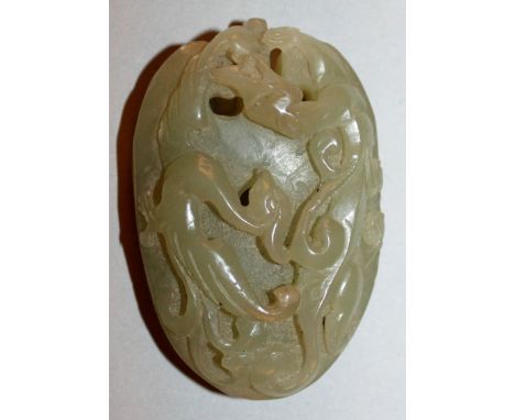 A CHINESE DARK CELADON JADE PENDANT, carved to its front in high relief with a dragon and a phoenix, 2.25in high.