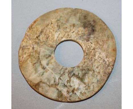 A CHINESE NEOLITHIC JADE BI DISC, the stone of predominantly pale green tone with brown inclusions, 4.7in diameter.