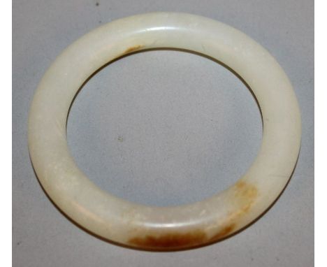 A CHINESE WHITE JADE-LIKE BANGLE, the stone with brown inclusions, 3.1in diameter, the inner rim 2.2in diameter.