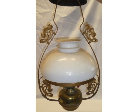 A brass hanging oil lamp with scroll shaped mounts and opaque glass shade