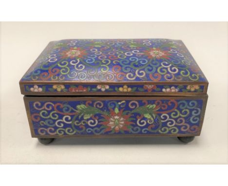 A Chinese cloisonné hinge-lidded rectangular box decorated with chrysanthemum amongst scrolls upon a dark blue ground and rai