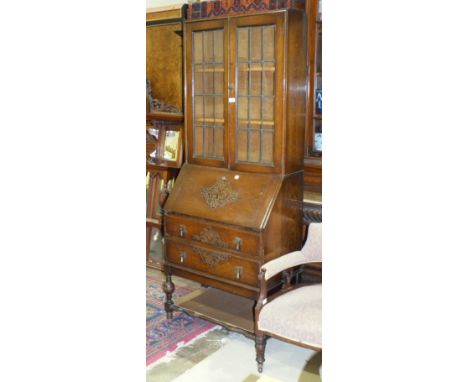 A 1950's oak bureau/bookcase, the upper shelved section fitted with a pair of leaded-light doors above a fall front and two d