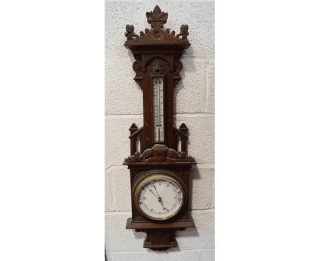 A late Victorian oak cased barometer and thermometer, carved with gothic and heraldic decoration, 108cm high