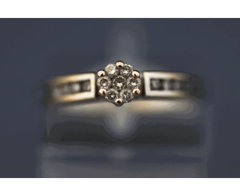 A diamond cluster ring, the white mount tagged '18K', the seven brilliant cut stones central cluster with a channel of four b
