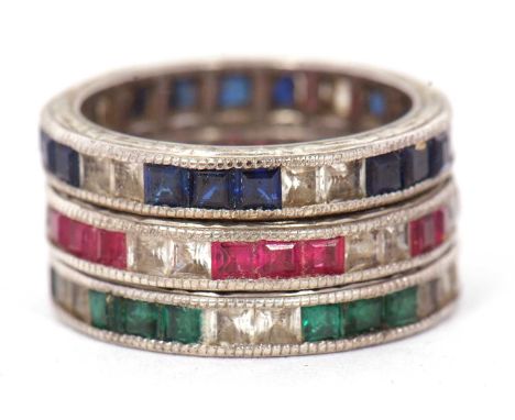 Three gemset eternity rings: to include a channel set sapphire and white stone ring with millegrain border and chased edges, 