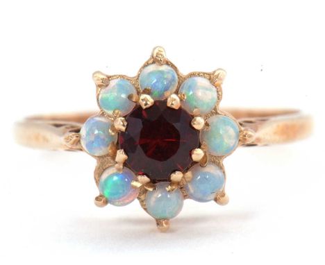 A 9ct opal and garnet ring, the central round garnet surrounded by small round cabochon opals, with plain band hallmarked Lon